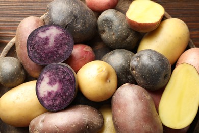 Photo of Different types of potatoes in bowl on wooden table, above view