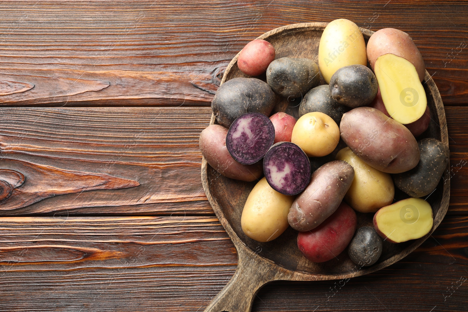 Photo of Different types of potatoes on wooden table, top view. Space for text