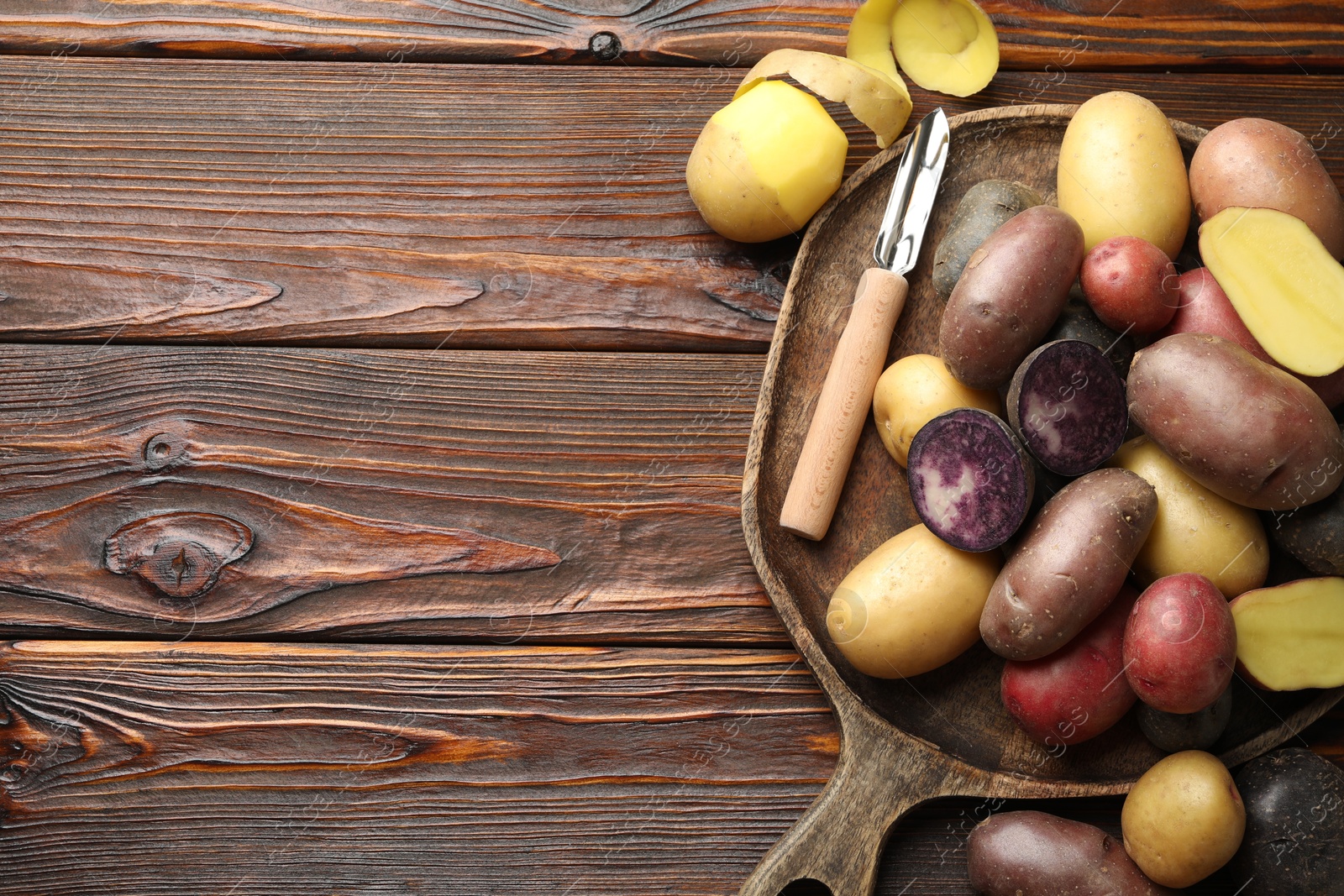 Photo of Different types of potatoes and peeler on wooden table, top view. Space for text