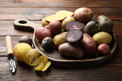 Photo of Different types of potatoes and peeler on wooden table, closeup
