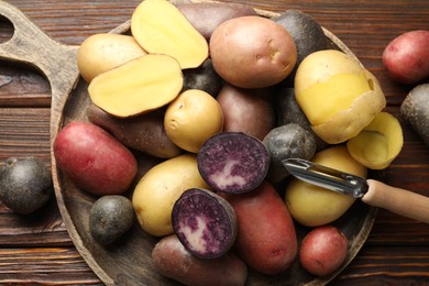 Photo of Different types of potatoes and peeler on wooden table, top view