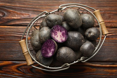 Photo of Raw purple potatoes in metal basket on wooden table, top view
