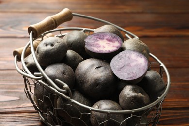 Photo of Raw purple potatoes in metal basket on wooden table, closeup