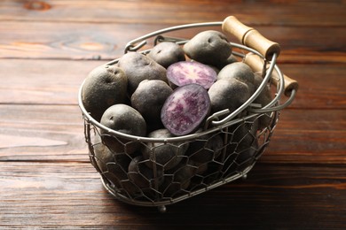 Photo of Raw purple potatoes in metal basket on wooden table, closeup