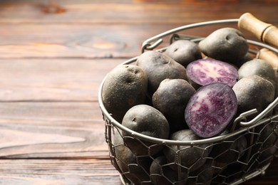 Photo of Raw purple potatoes in metal basket on wooden table, closeup. Space for text