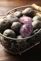 Photo of Raw purple potatoes in metal basket on wooden table, closeup