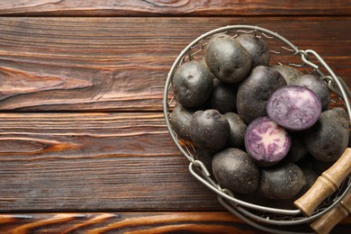 Photo of Raw purple potatoes in metal basket on wooden table, top view. Space for text