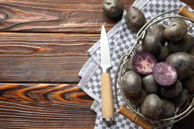 Photo of Raw purple potatoes in metal basket and knife on wooden table, flat lay. Space for text