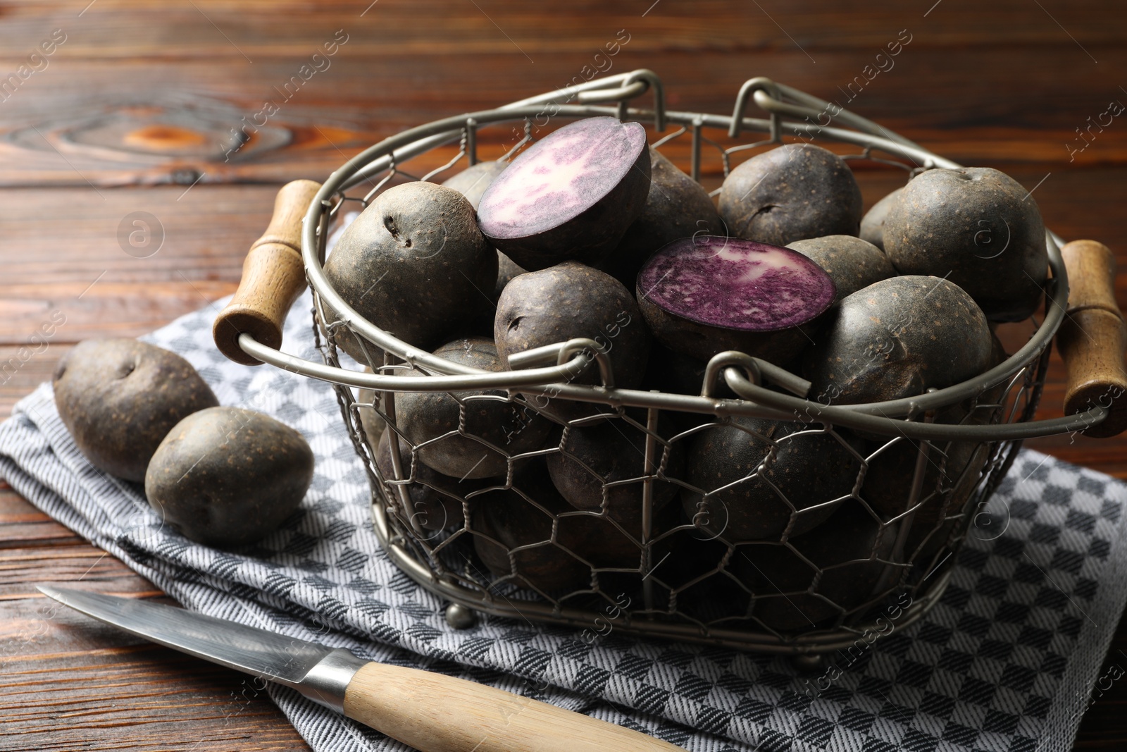 Photo of Raw purple potatoes in metal basket and knife on wooden table, closeup