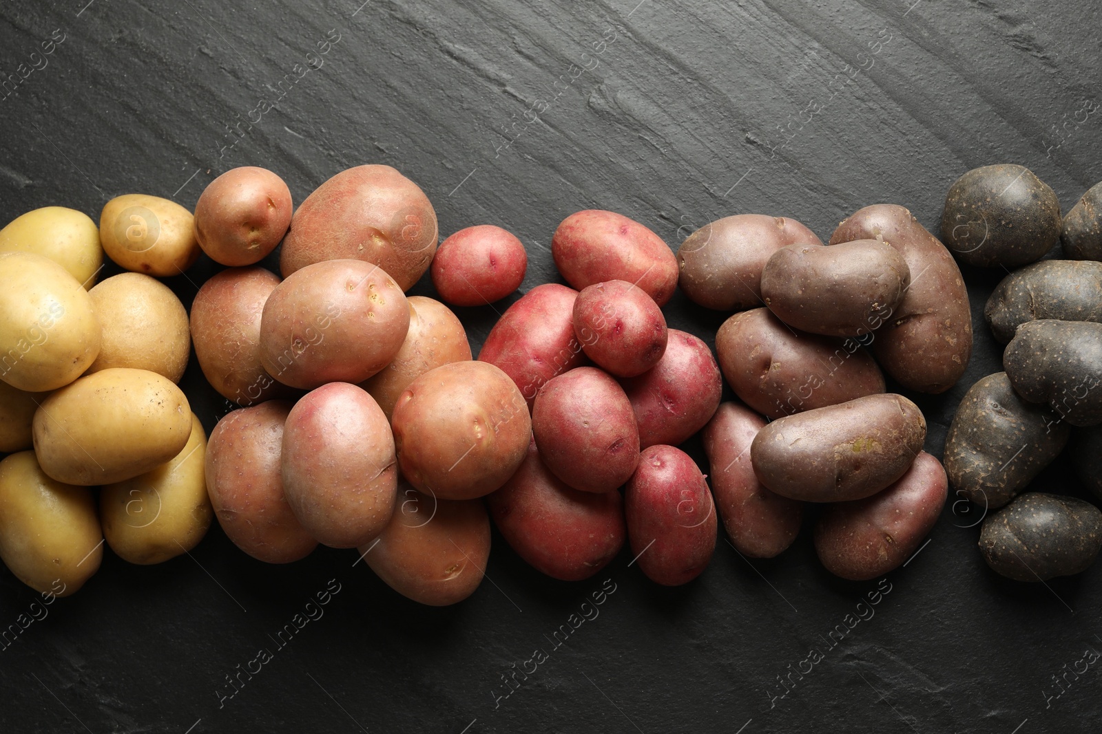 Photo of Different types of potatoes on black table, flat lay