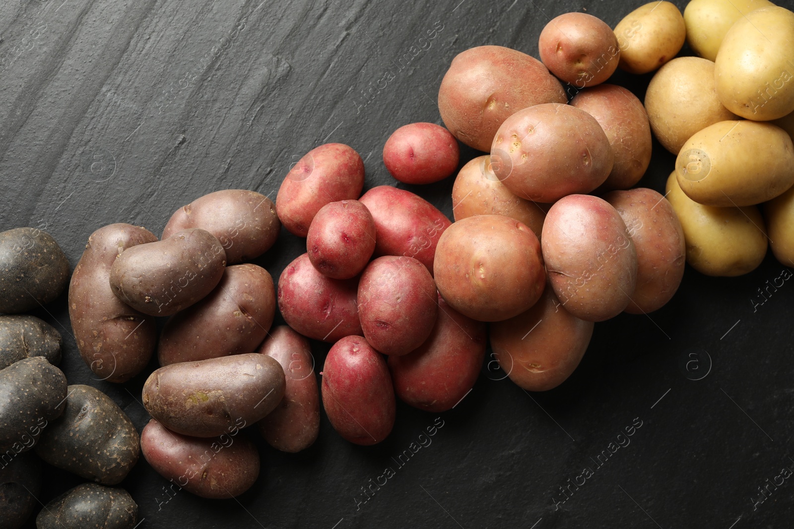 Photo of Different types of potatoes on black table, flat lay