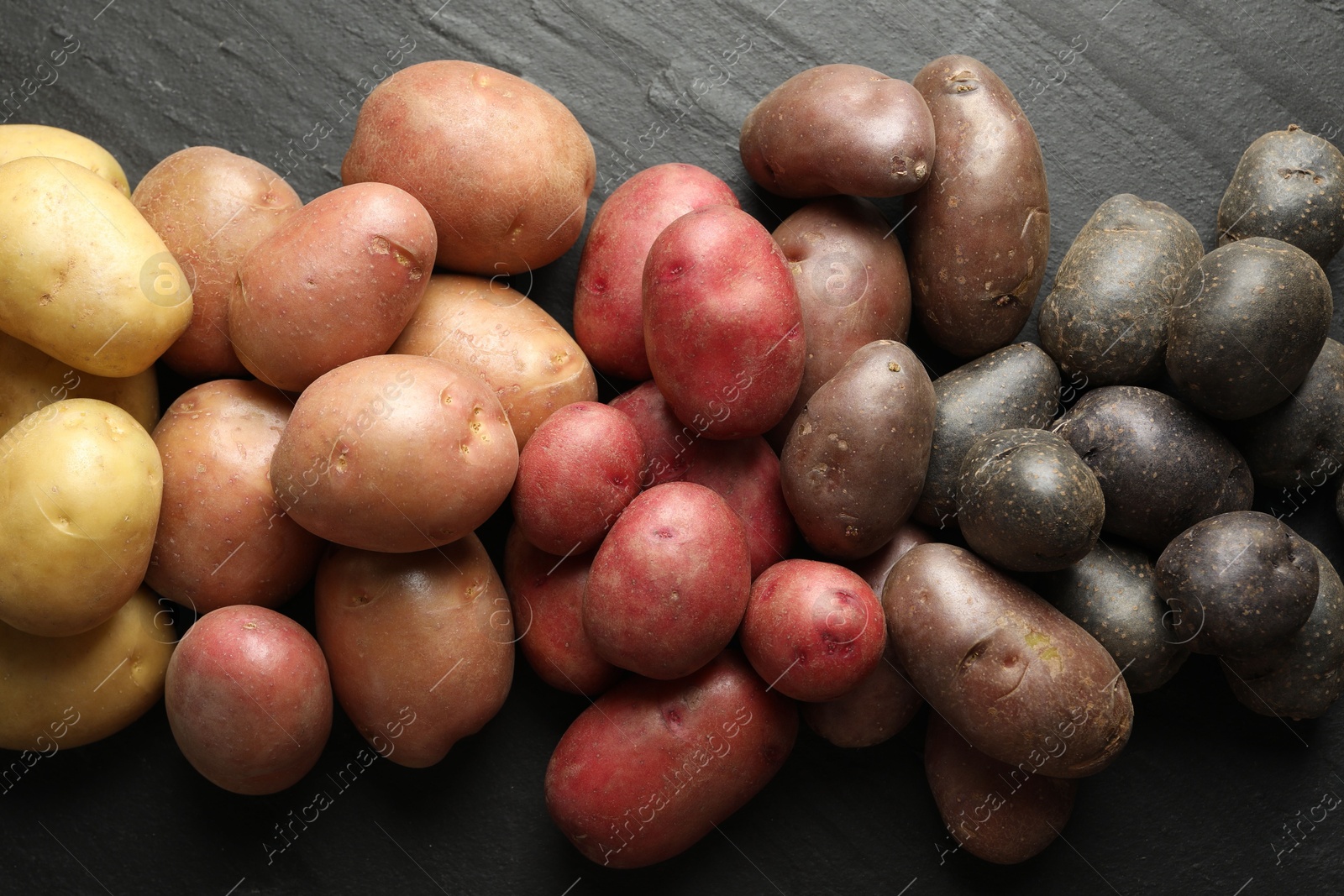 Photo of Different types of potatoes on black table, flat lay