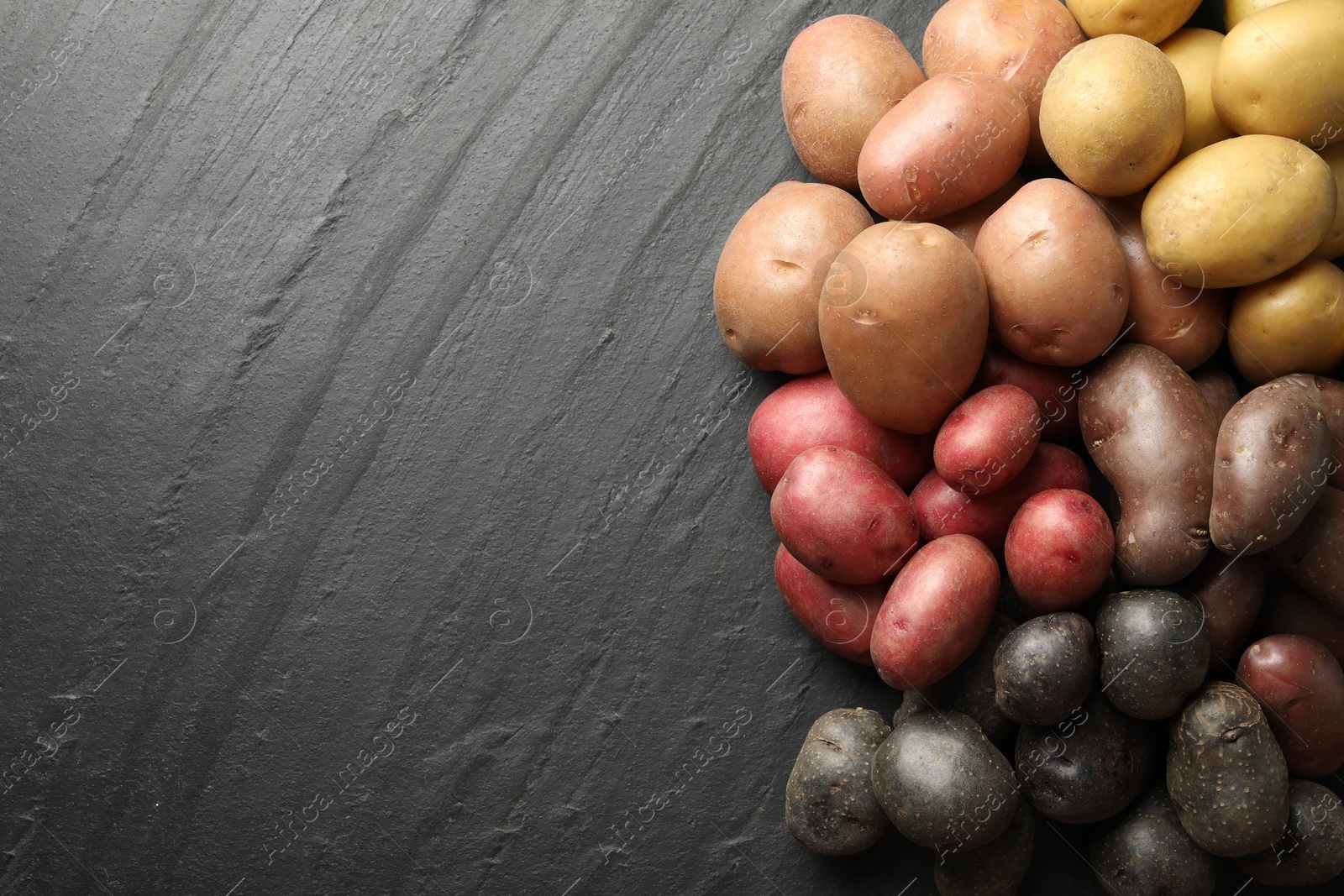 Photo of Different types of potatoes on black table, flat lay. Space for text