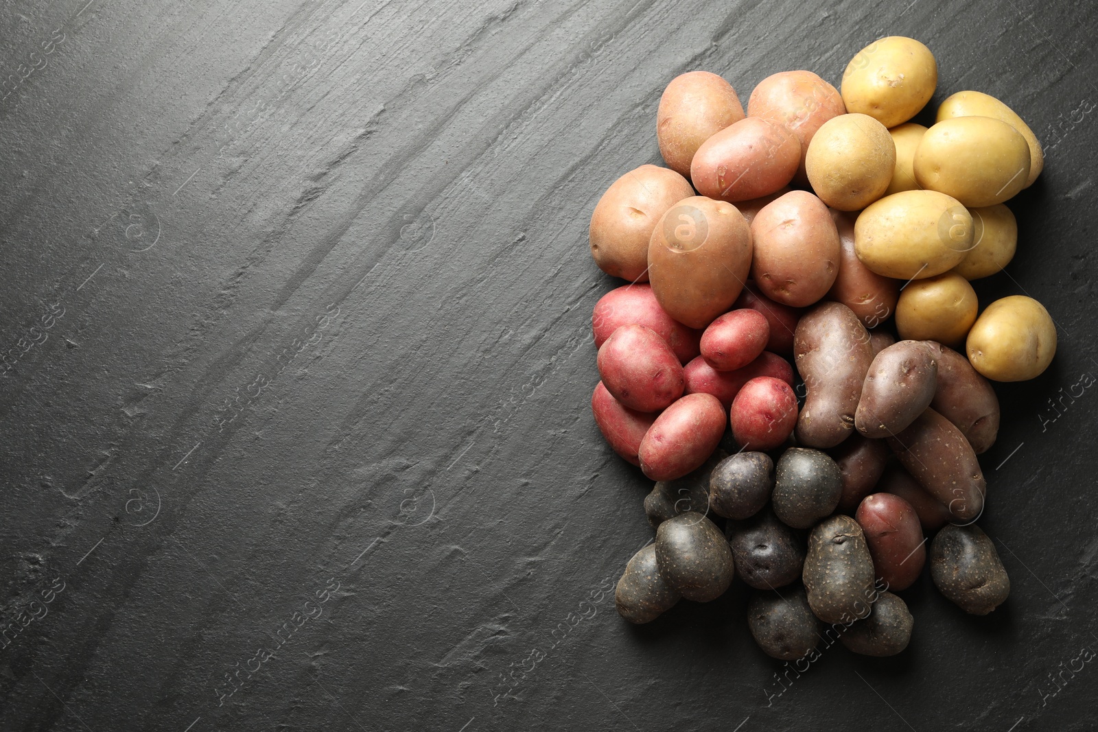 Photo of Different types of potatoes on black table, flat lay. Space for text