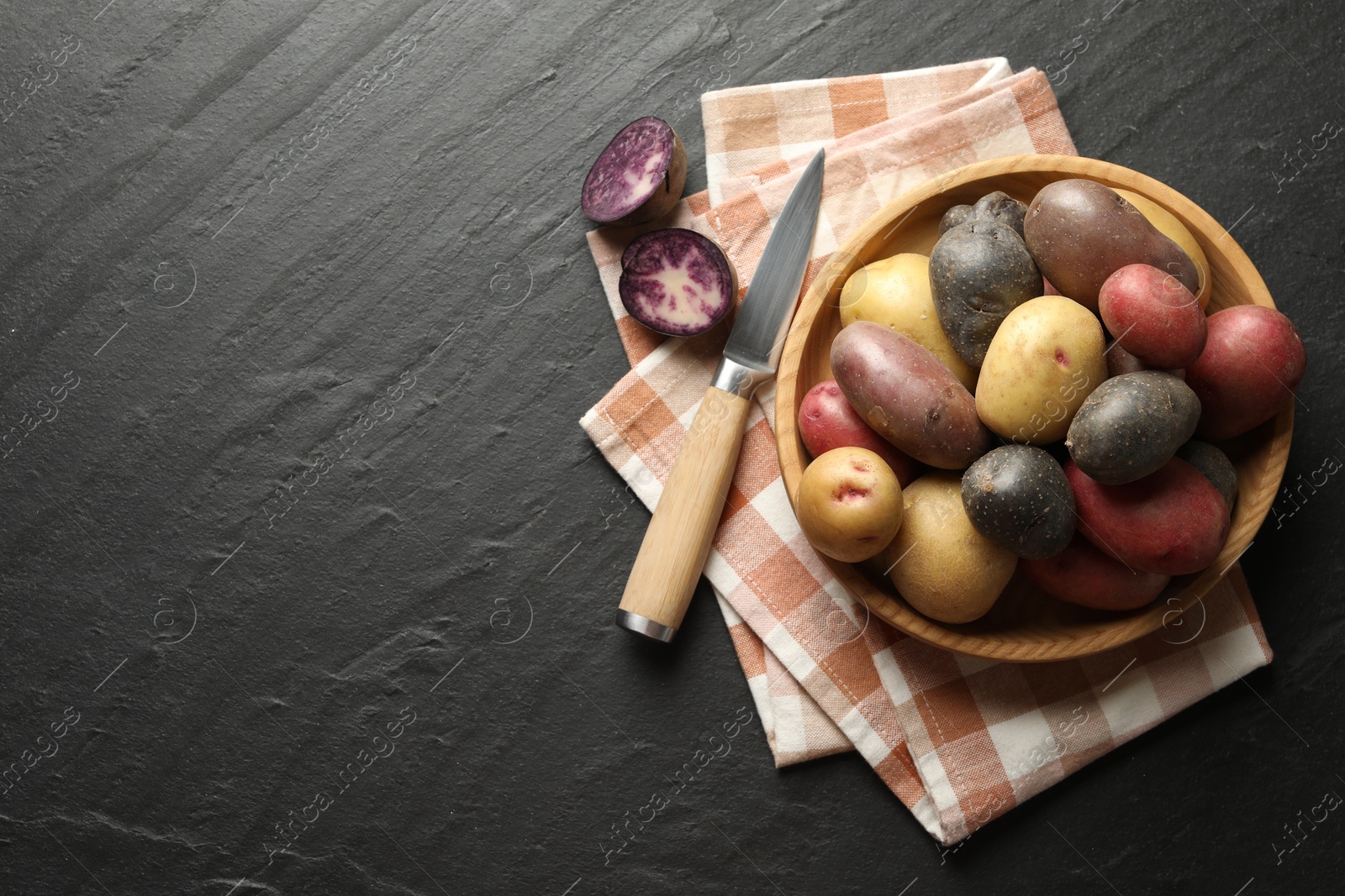 Photo of Different types of potatoes in bowl and knife on black table, flat lay. Space for text