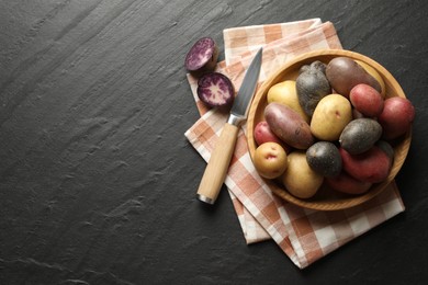 Photo of Different types of potatoes in bowl and knife on black table, flat lay. Space for text
