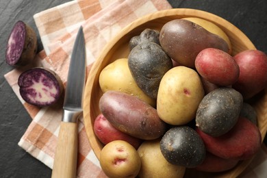 Photo of Different types of potatoes in bowl and knife on black table, flat lay