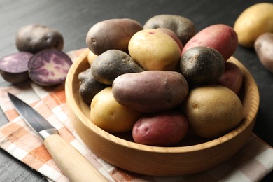 Photo of Different types of potatoes in bowl and knife on black table, closeup