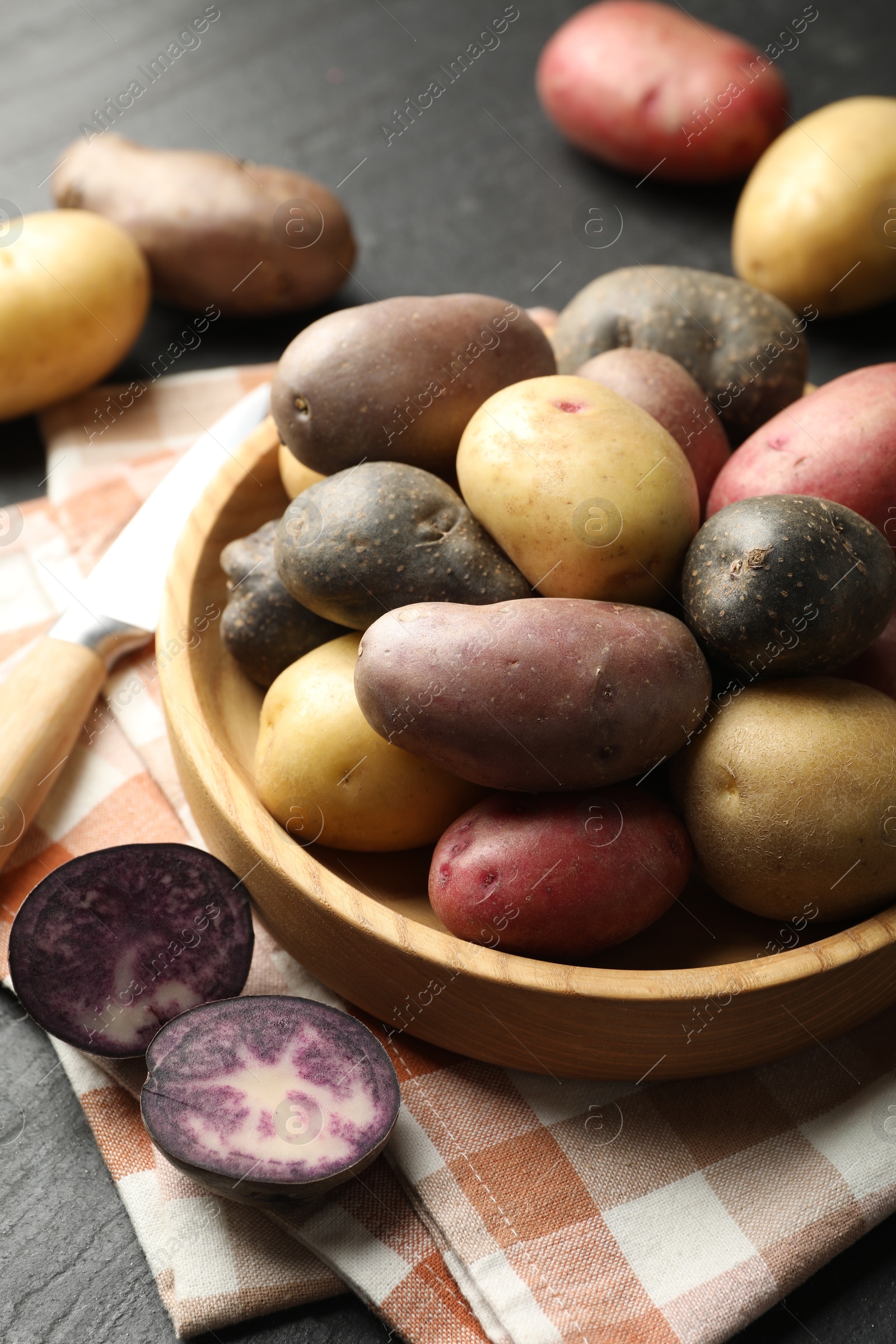 Photo of Different types of potatoes in bowl and knife on black table, closeup