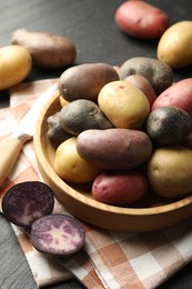 Photo of Different types of potatoes in bowl and knife on black table, closeup