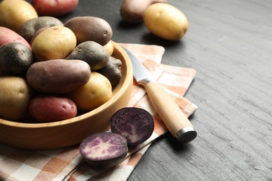 Photo of Different types of potatoes in bowl and knife on black table, closeup. Space for text