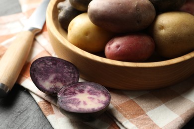 Photo of Different types of potatoes in bowl and knife on black table, closeup