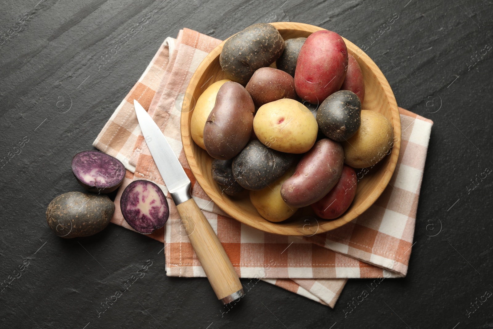 Photo of Different types of potatoes in bowl and knife on black table, flat lay