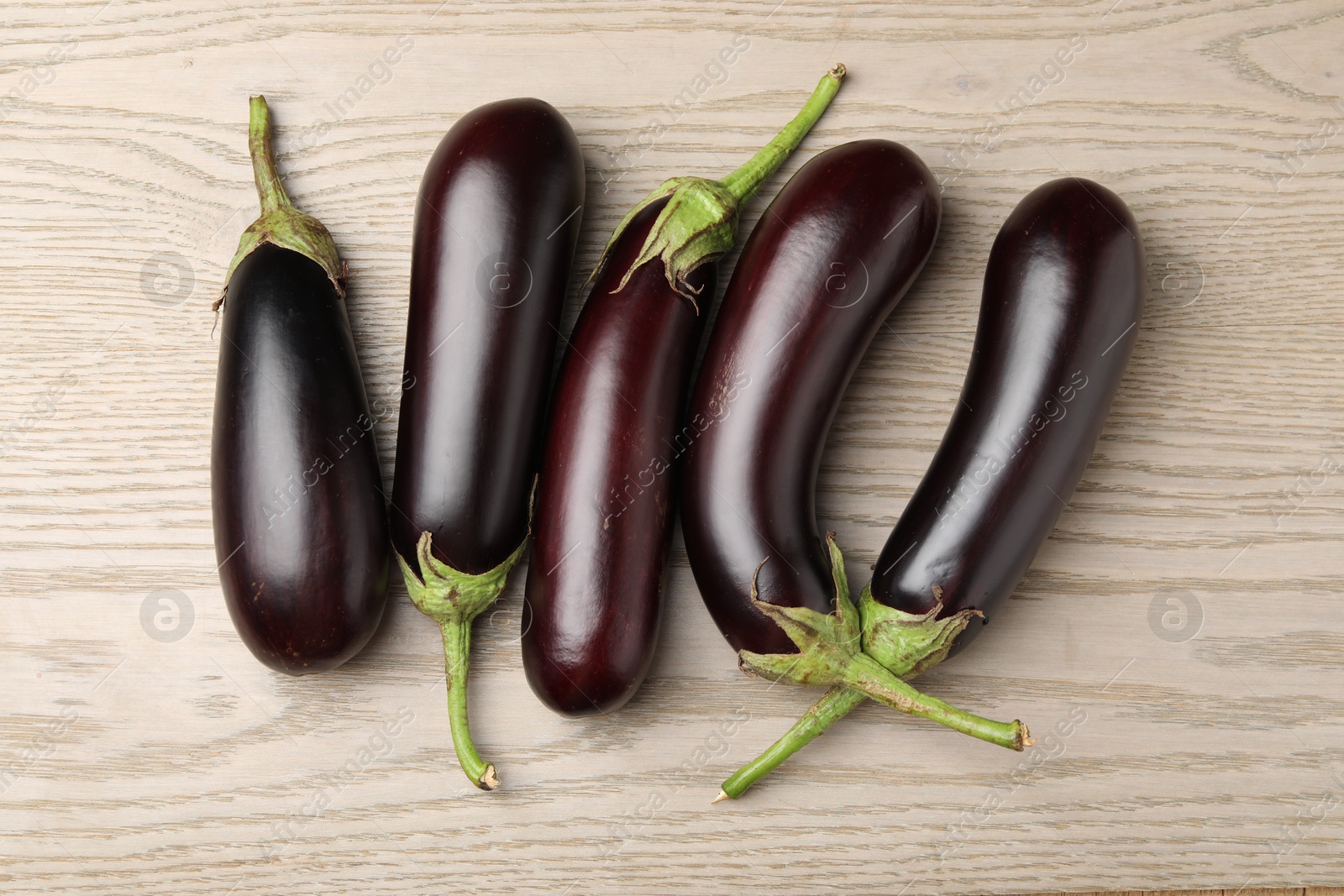 Photo of Many ripe eggplants on light wooden table, flat lay