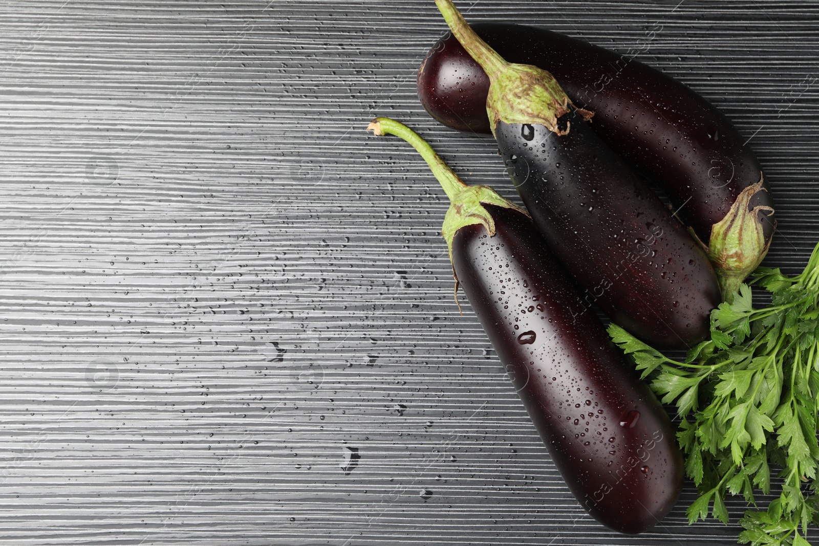 Photo of Many wet ripe eggplants with parsley on black wooden table, top view. Space for text