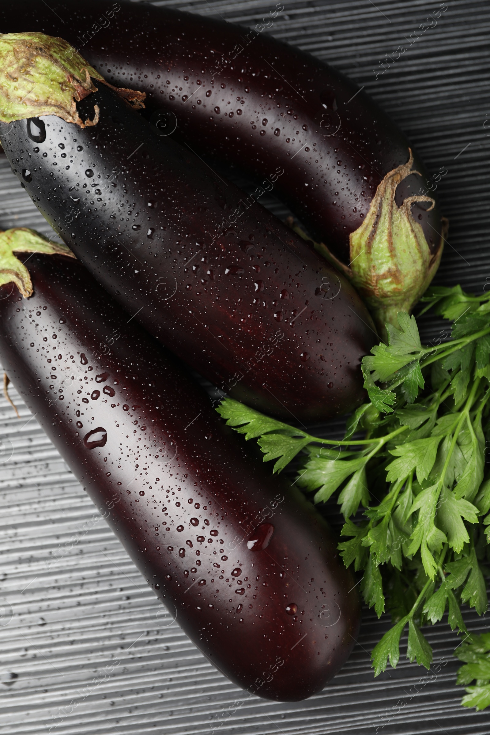 Photo of Many wet ripe eggplants with parsley on black wooden table, closeup