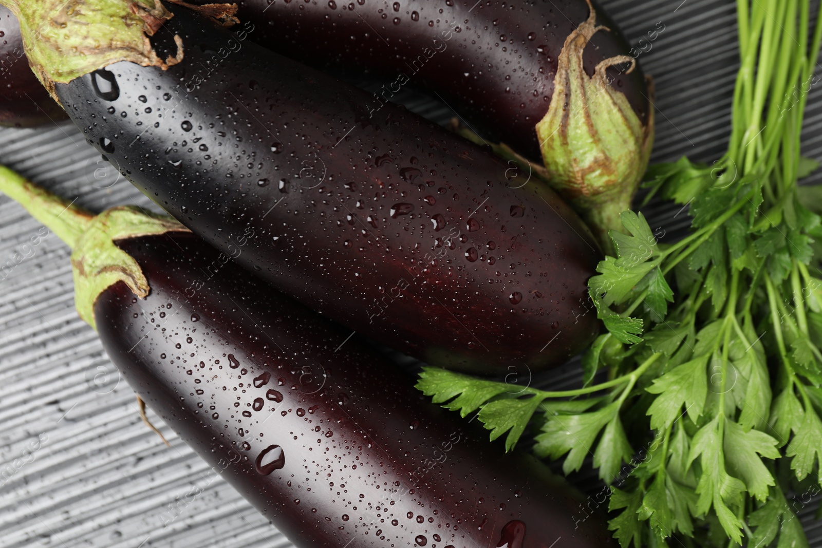 Photo of Many wet ripe eggplants with parsley on black wooden table, closeup