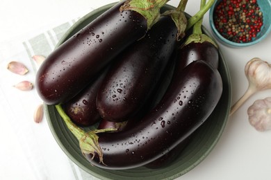 Photo of Many wet ripe eggplants, peppercorns and garlic on white table, flat lay