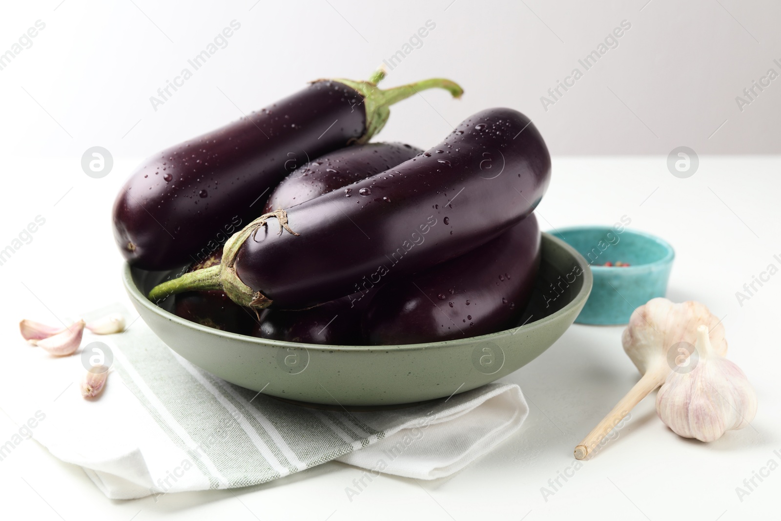 Photo of Many wet ripe eggplants and garlic on white table
