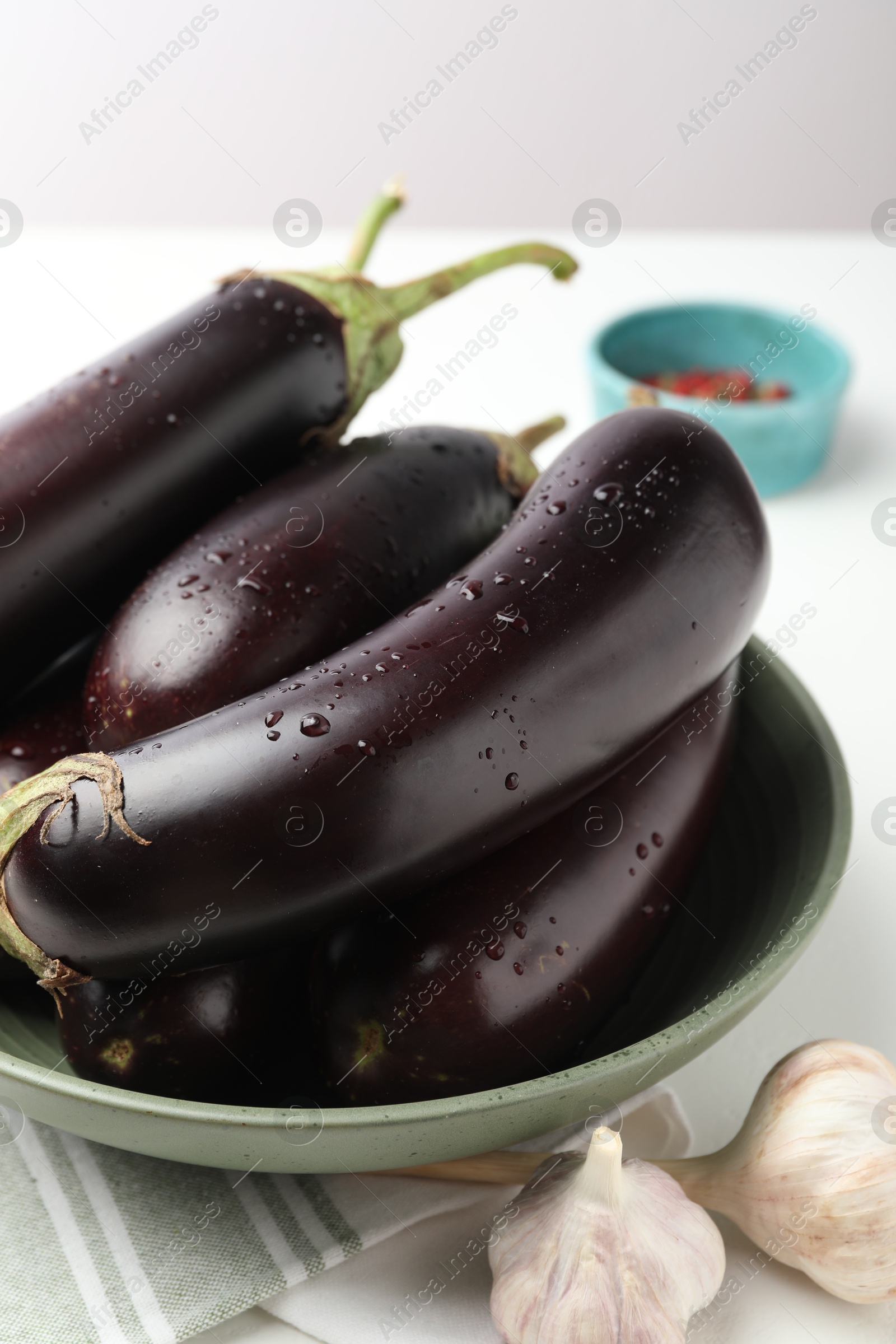 Photo of Many wet ripe eggplants and garlic on white table, closeup