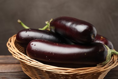 Photo of Many ripe eggplants in basket on wooden table, closeup