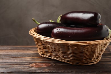 Photo of Many ripe eggplants in basket on wooden table