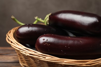 Photo of Many ripe eggplants in basket on wooden table, closeup