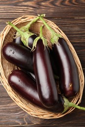 Photo of Many ripe eggplants in basket on wooden table, top view