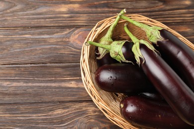 Photo of Many ripe eggplants in basket on wooden table, top view. Space for text