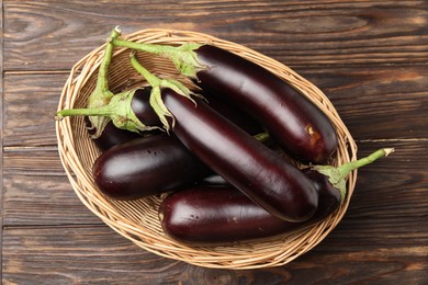 Photo of Many ripe eggplants in basket on wooden table, top view
