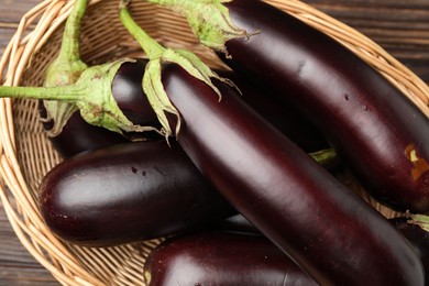 Photo of Many ripe eggplants in basket on wooden table, closeup