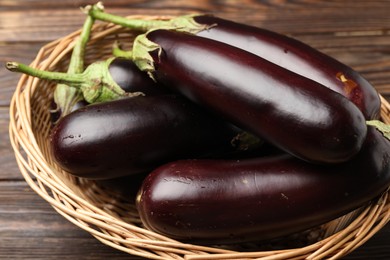 Photo of Many ripe eggplants in basket on wooden table, closeup