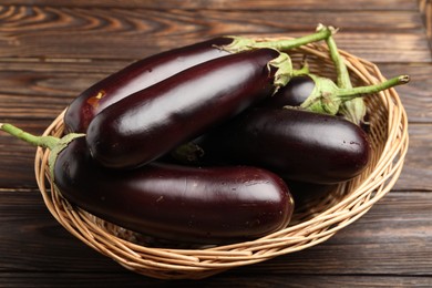 Photo of Many ripe eggplants in basket on wooden table, closeup