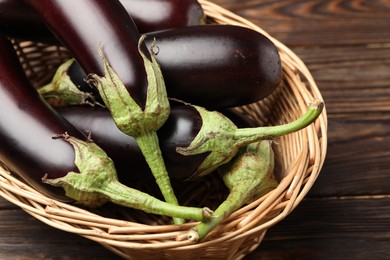 Photo of Many ripe eggplants in basket on wooden table, closeup