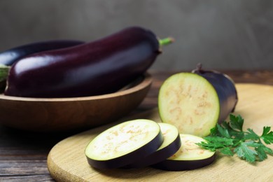 Photo of Whole and cut eggplants with parsley on wooden table, closeup