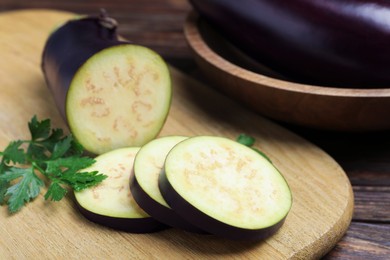 Photo of Whole and cut eggplants with parsley on wooden table, closeup