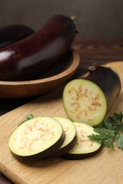 Photo of Whole and cut eggplants with parsley on wooden table, closeup