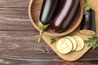 Photo of Whole and cut eggplants with parsley on wooden table, flat lay. Space for text
