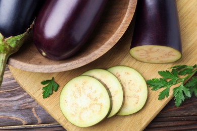 Photo of Whole and cut eggplants with parsley on wooden table, flat lay