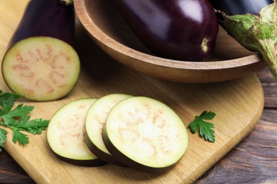 Photo of Whole and cut eggplants with parsley on wooden table, closeup